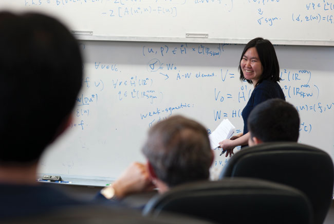 Professor giving lecture in front of white boards with covered with equations