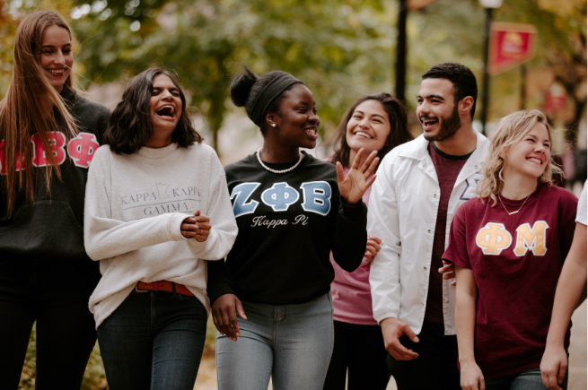 Students of different races and ethnicities wearing sweatshirts from various sororities and fraternities on campus