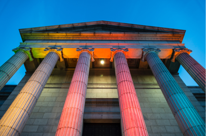 Ionic columns of Minneapolis Institute of Arts lit from below in rainbow colors with dark night sky behind