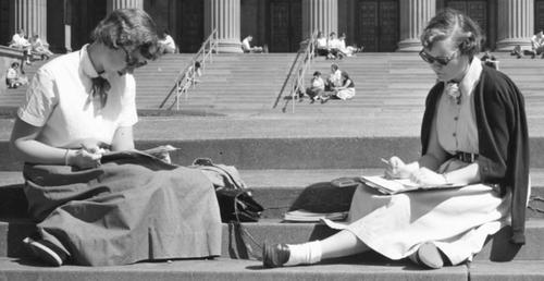 black and white image of two young female students studying on the plaza with Northrop visible in background