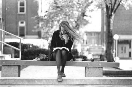 Young woman studying on stone bench on campus 