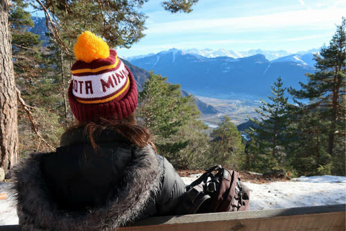 student wearing U of M winter hat looking out at mountain scene