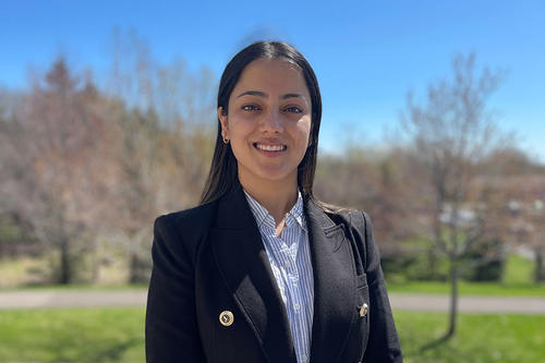 Lujana Thapa wearing a suit with two pins and a button up shirt on campus smiling