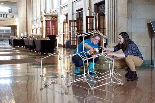 In a well-lit Northrop lobby, two female students construct a model of a diamond crystal.